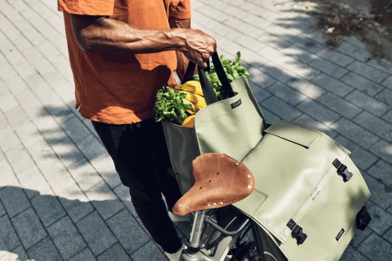 Een persoon zet boodschappen in een lichtgroene Clarijs-fietstas op een fiets.