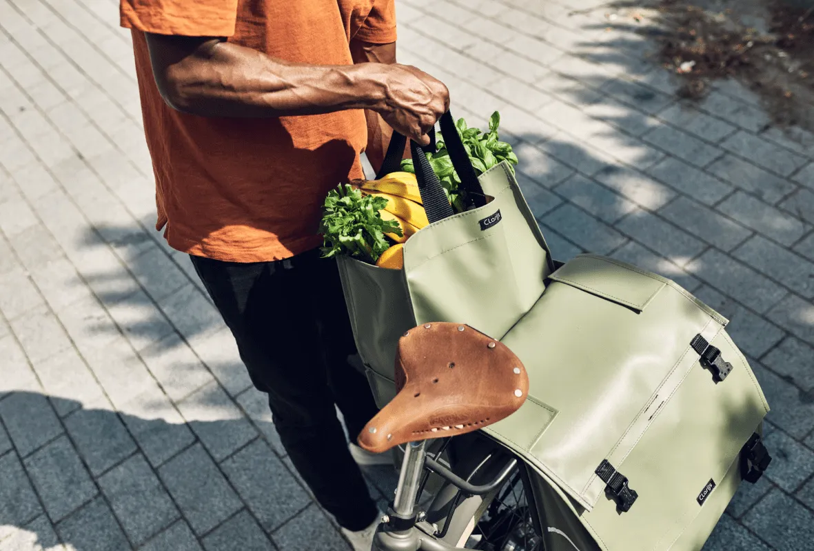 Een persoon zet boodschappen in een lichtgroene Clarijs-fietstas op een fiets.